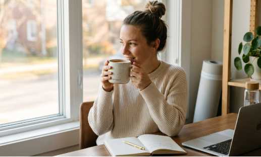 person holding ceramic coffee mug in morning routine with sunlight and minimal workspace